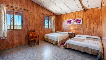 Una habitación con paredes de madera, dos camas, una silla y un ventanal con cortinas.