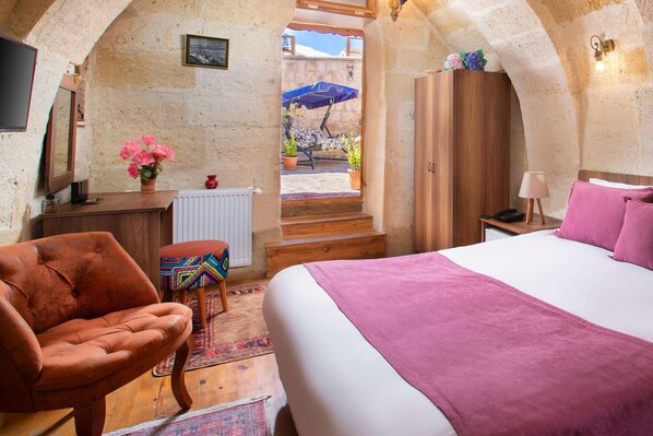 A cozy bedroom with a bed, a chair, a wooden desk, a radiator, and a view of the outside.