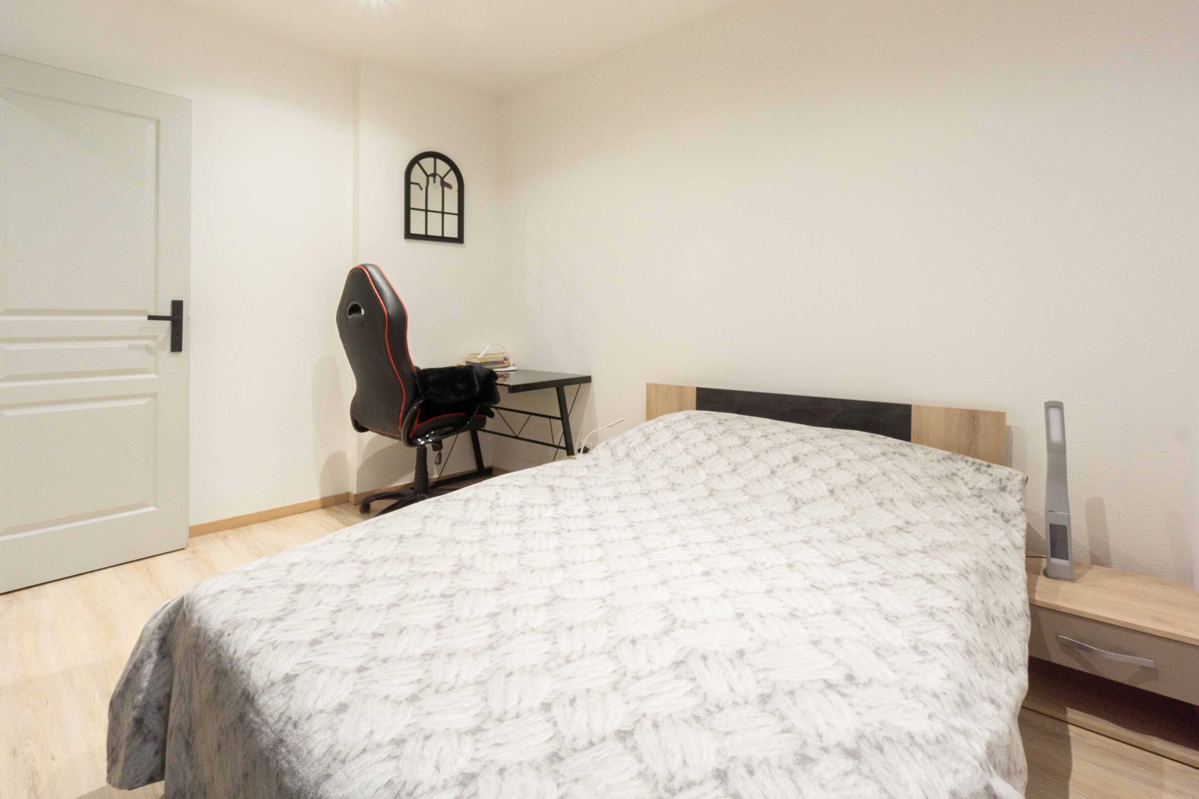 A bedroom with a bed, a desk, and a chair.