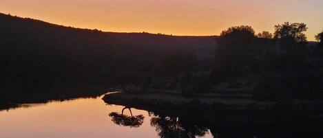 Un llac tranquil a la posta de sol amb el reflex clar dels arbres i les colines.