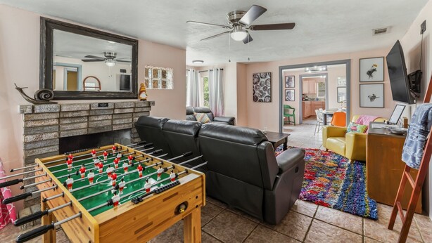 Una sala de estar con una mesa de fútbol de mesa, una chimenea, un ventilador de techo y un televisor.