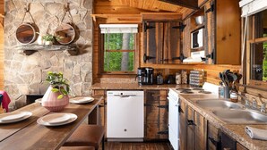 Una cocina rústica con paredes de piedra, vigas de madera, un lavavajillas blanco, una estufa y un ventanal grande.