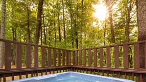 Un jacuzzi rodeado por una terraza de madera con un bosque al fondo.