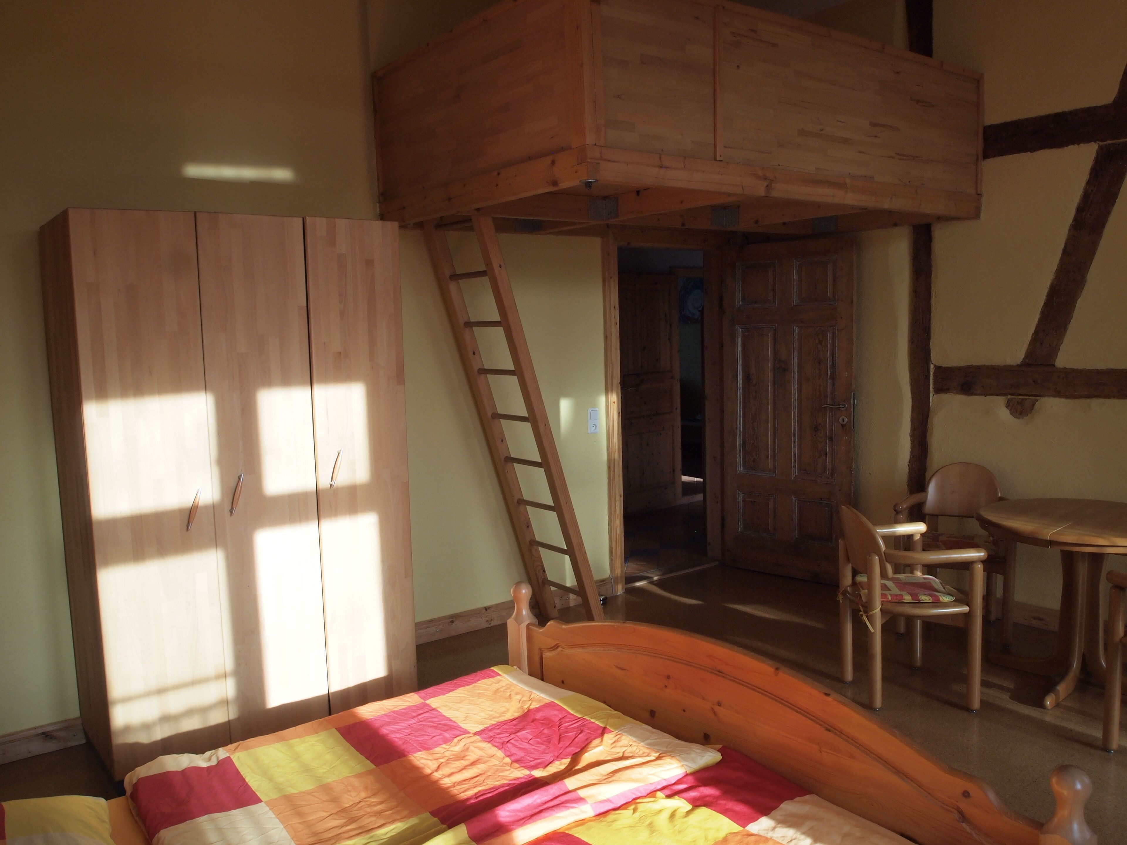 Een slaapkamer met een hoogslaper, een houten ladder, een bureau en een stoel.