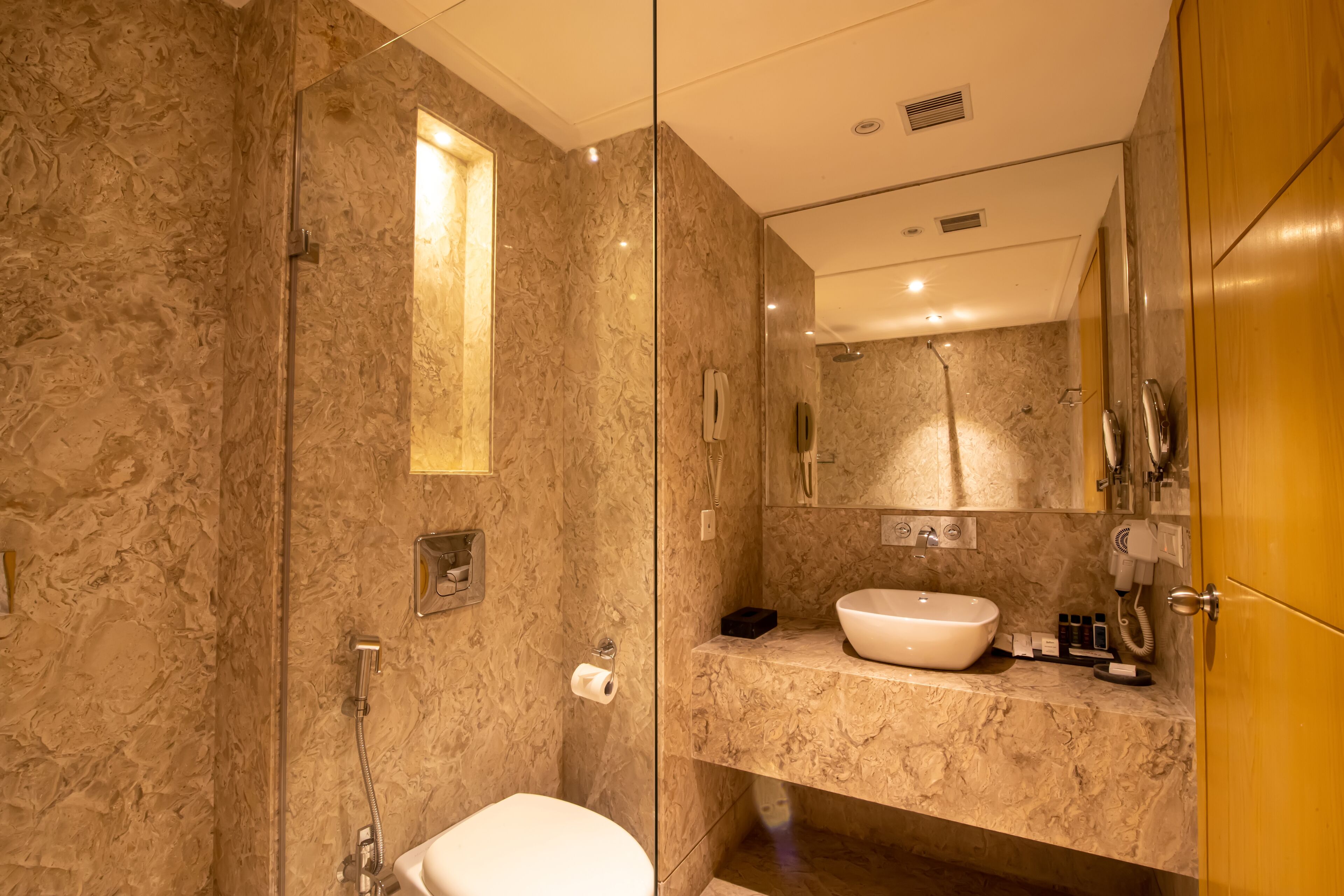 Un baño moderno con ducha envuelta en vidrio, lavamanos de mármol y tocador con espejo.