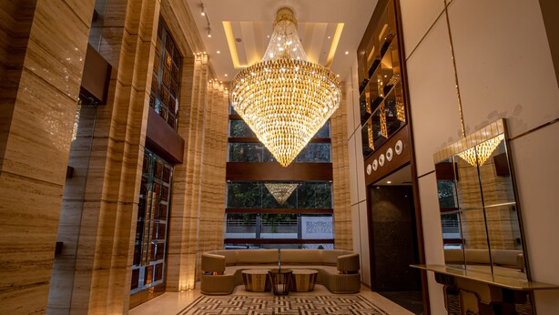 Un hall d’entrée luxueux, agrémenté d’un imposant lustre, d’un espace salon et d’un grand miroir qui reflète l’ensemble de la pièce.