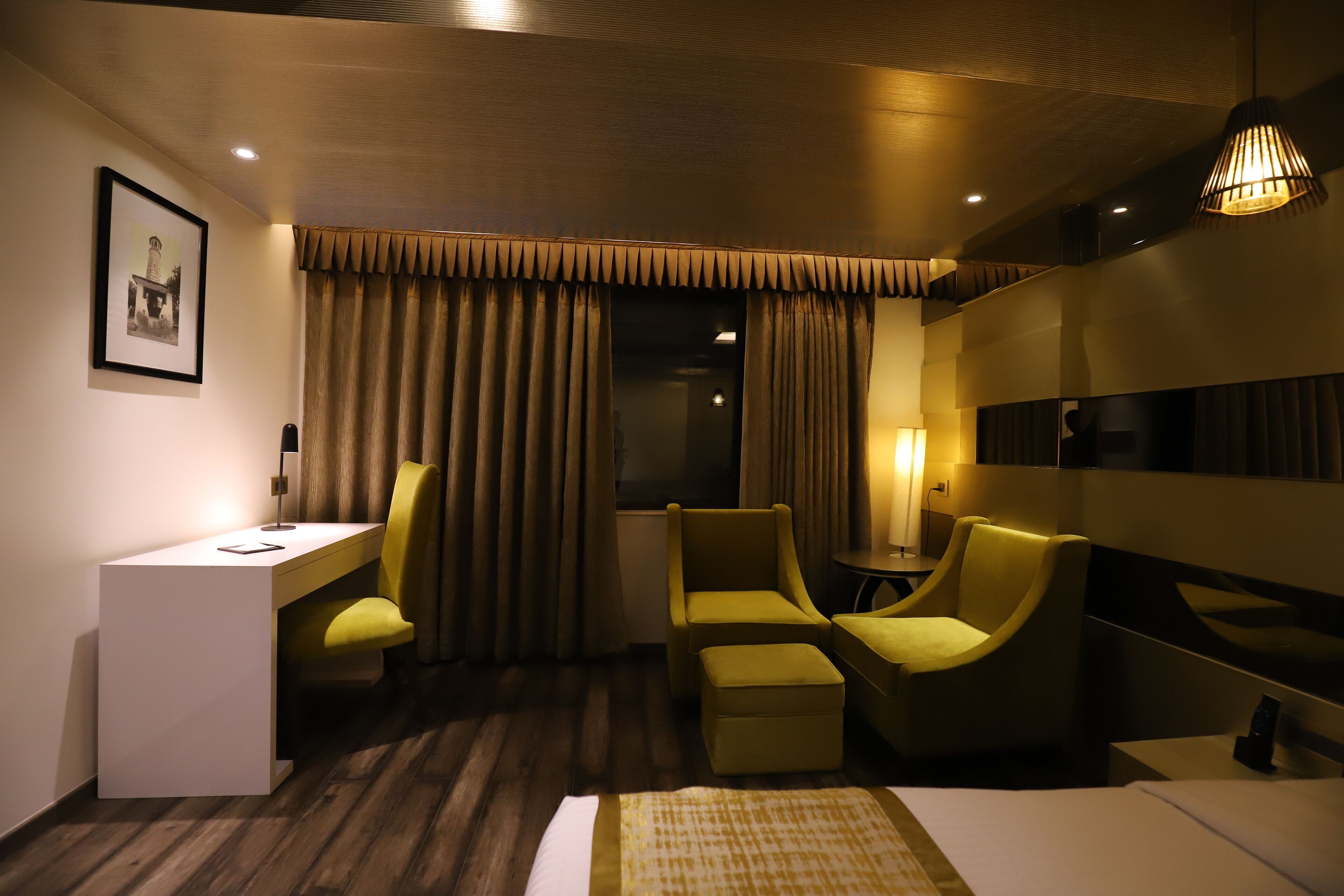Habitación de hotel con escritorio, dos sillones, una mesita, cama y un gran ventanal con cortinas.