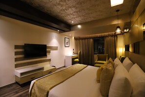 A modern hotel room with a large bed, a flat-screen TV mounted on the wall, a desk with a chair, and a window with curtains. - The Pristine Hotel Kanpur (Kanpur)