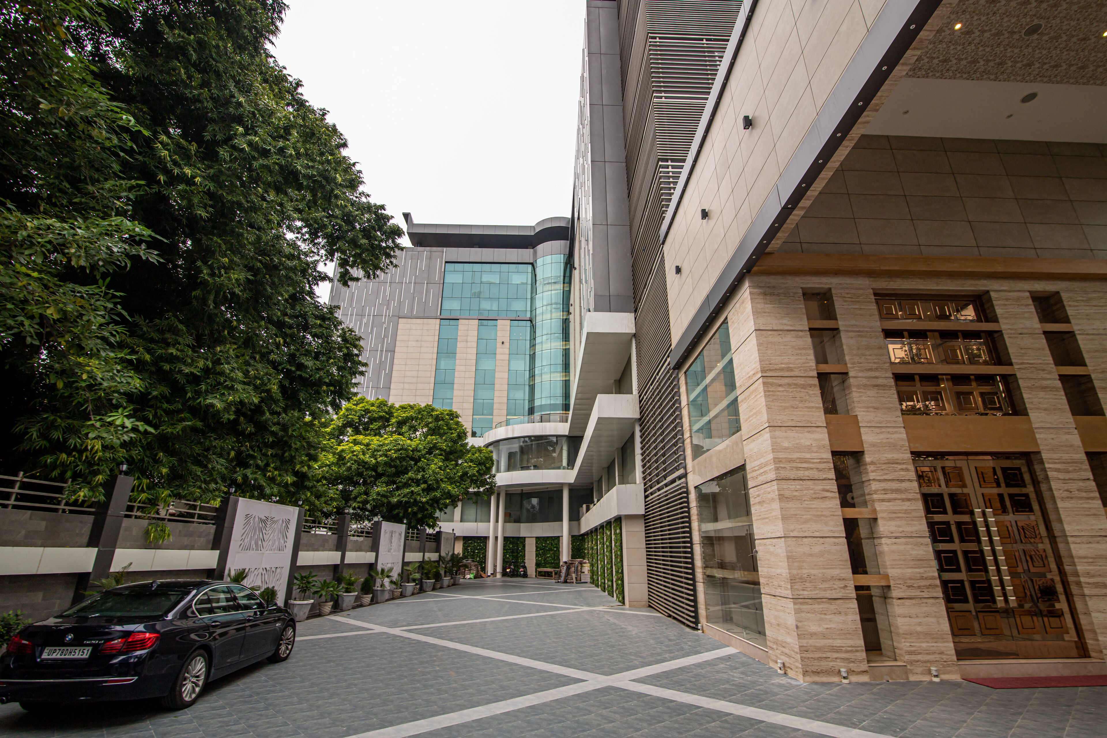 Un edificio moderno con fachada de vidrio curva, un patio empedrado y un coche aparcado.