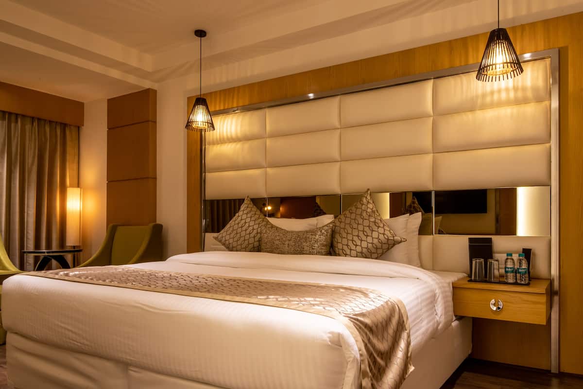 Habitació d'hotel amb un llit gran, una taula de nit amb un mirall i una cadira verda.