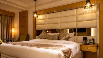 A hotel room with a large bed, a bedside table with a mirror, and a green chair.