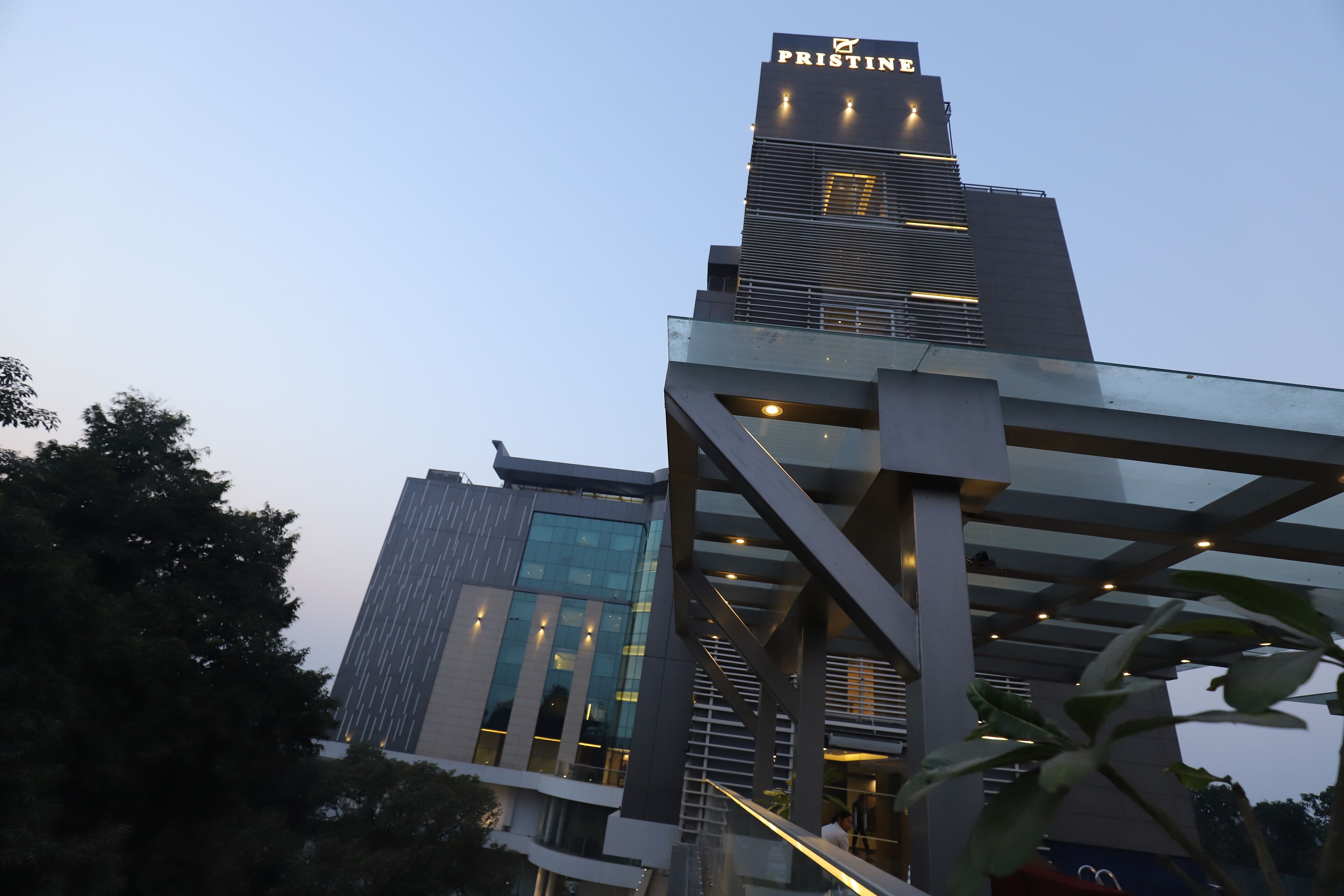 A modern building with the sign 'PRISTINE' at the top. It features a glass facade and a metal structure in the foreground.