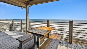 Une terrasse en bois avec une table et des bancs donnant sur une plage.