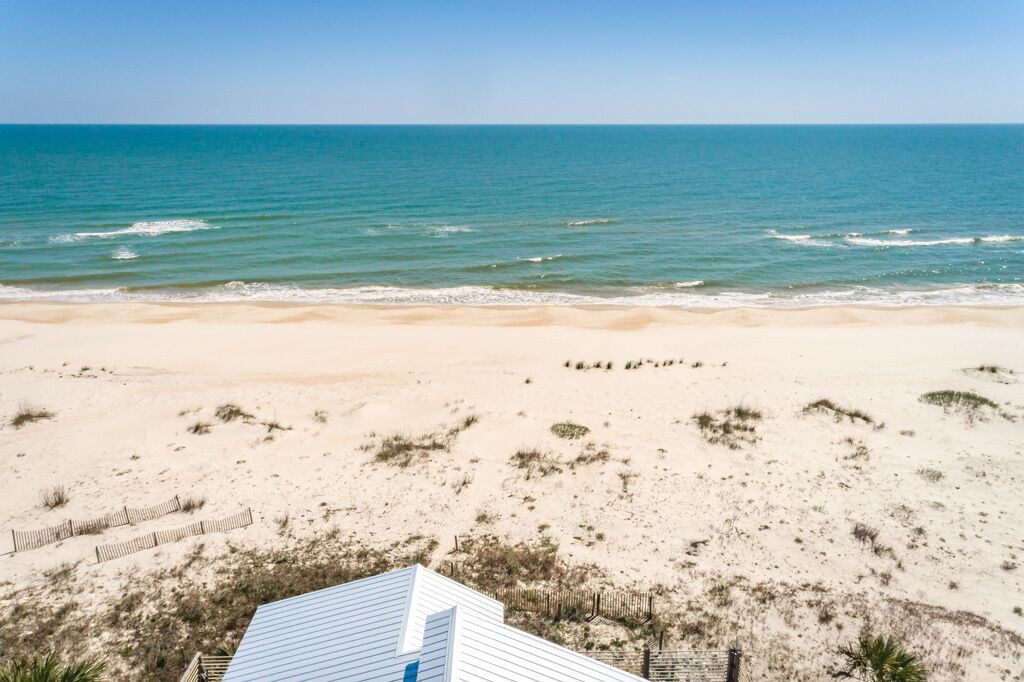 A beach view with a sandy landscape, a wooden fence, and a building with a blue roof.