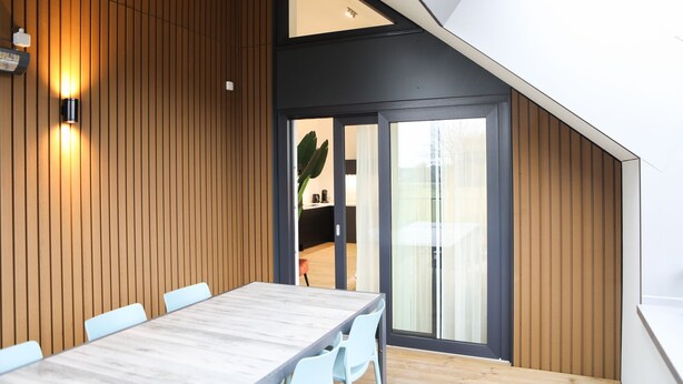 Un comedor moderno con pared de madera, una mesa grande y sillas de color claro.