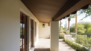 A covered walkway with a view of a garden and palm trees.