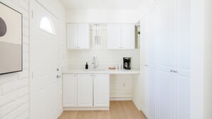 A small, white kitchen with white cabinets, a wooden countertop, and a coffee maker.