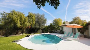 A swimming pool with lounge chairs and an umbrella, surrounded by a well-maintained lawn and trees.