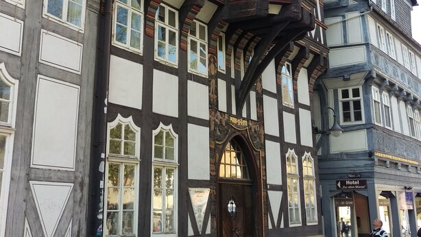 A traditional half-timbered building with a prominent corner tower, large windows, and a wooden door with a sign above it. - Modern apartment with WLAN in the old town (near the market square) (Goslar)