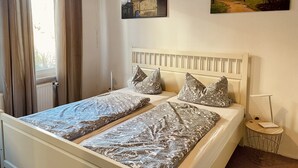 A double bed with patterned bedding, a bedside table, a lamp, and two wall paintings. - Modern apartment with WLAN in the old town (near the market square) (Goslar)