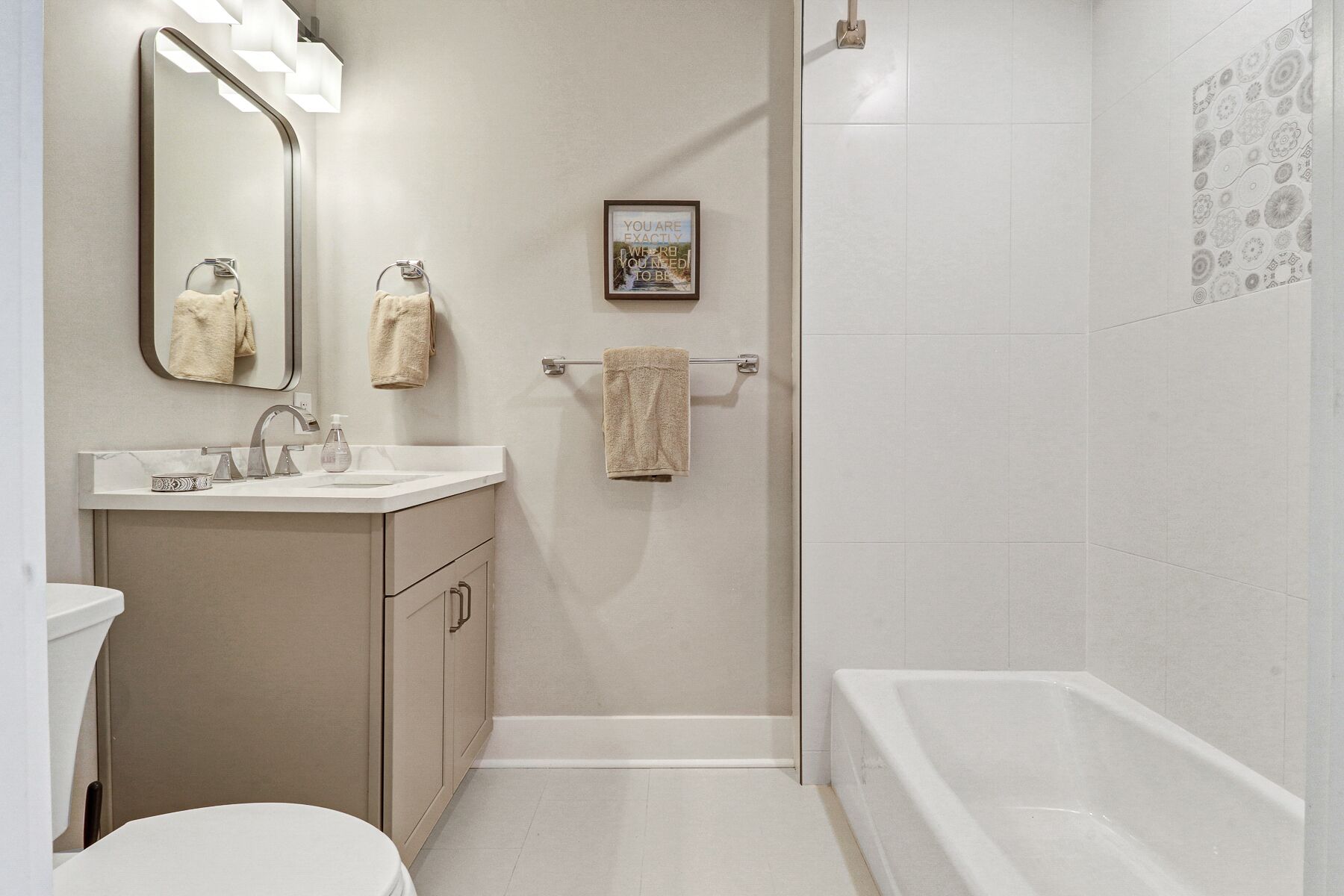 A modern bathroom with a white sink, mirror, and bathtub. There are two towels hanging on towel bars.