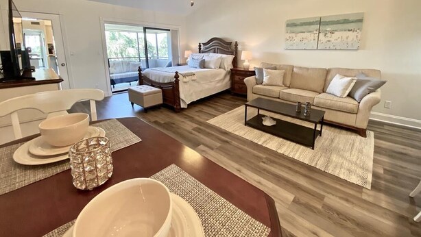 A spacious living room with a large bed, a sofa, a dining table with chairs, and a ceiling fan.