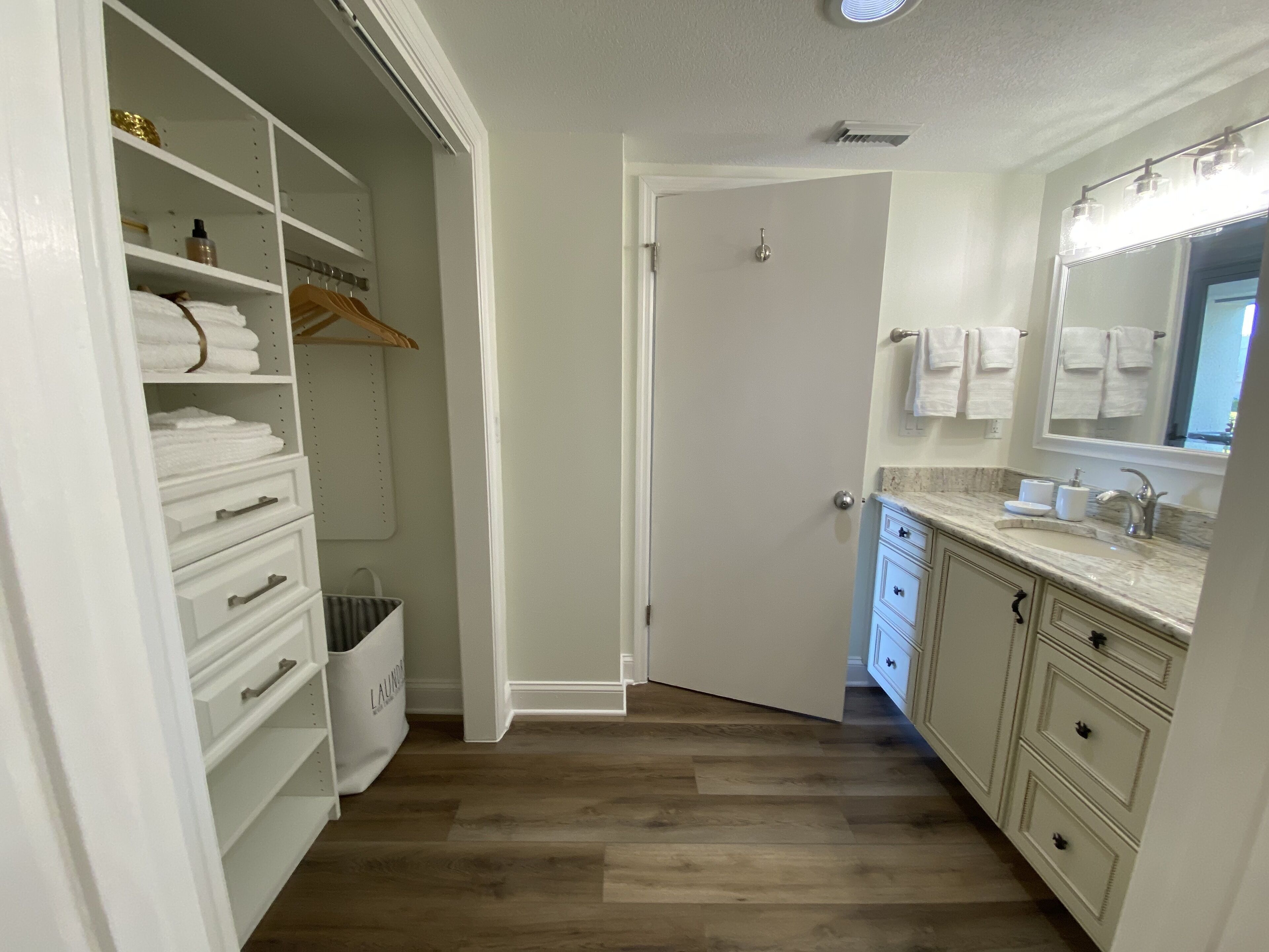 A clean, modern bathroom with a vanity, sink, and mirror. There is a walk-in closet with shelves and drawers.