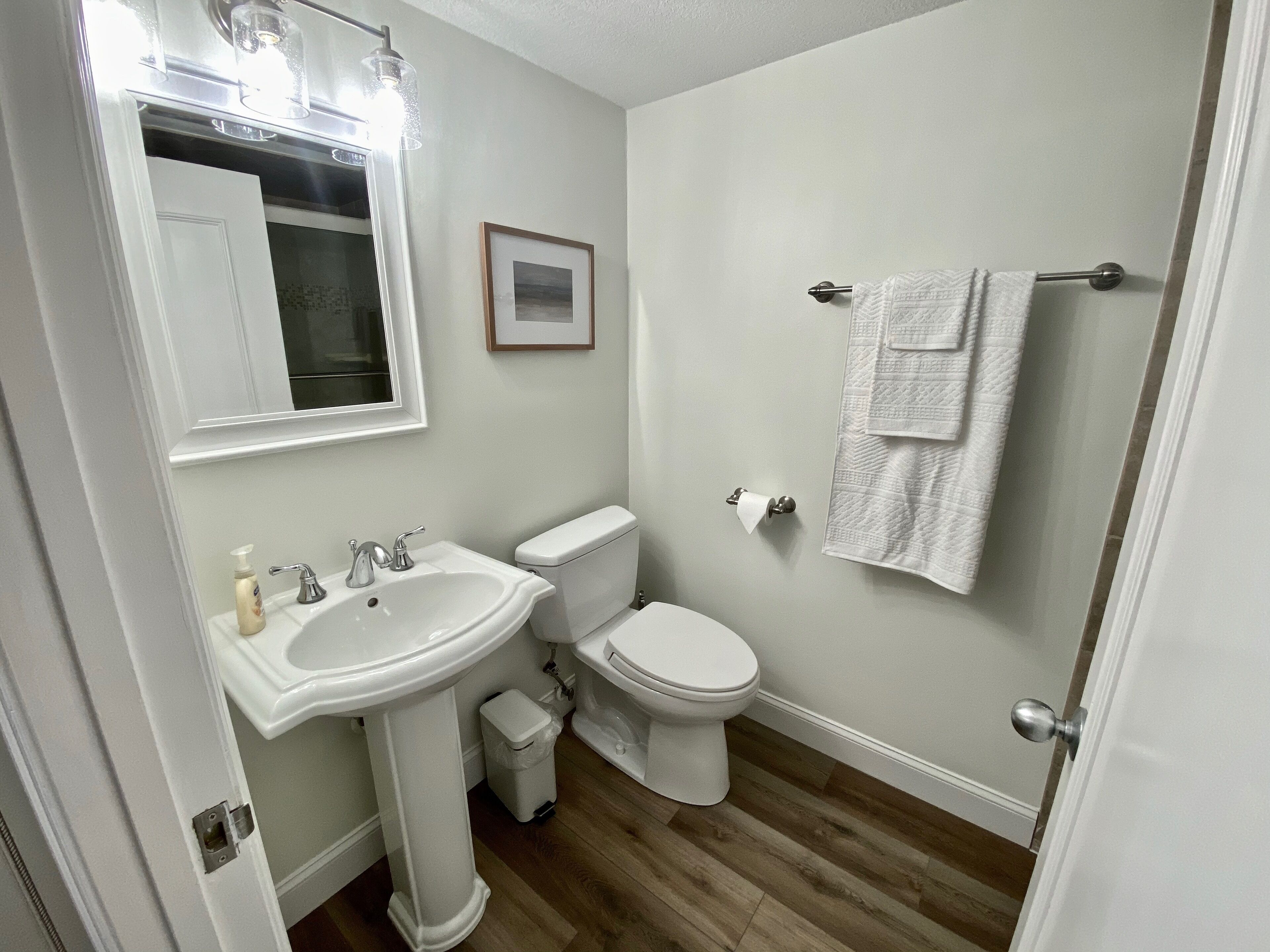 A bathroom with a pedestal sink, a toilet, a framed picture on the wall, and a towel rack with towels.