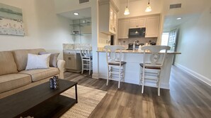 A modern living room with a sofa, coffee table, and a kitchen area with bar stools and a microwave.