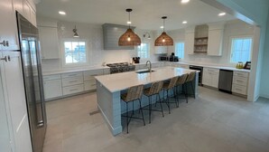 A modern kitchen with a large island, white cabinetry, and pendant lighting.