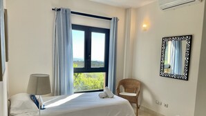 A hotel room with two beds, a chair, a table, a lamp, a mirror, and a window with curtains. - Villa Over the 5th Green (San Bartolomé de Tirajana)