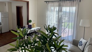 Un salon moderne avec un canapé, une table à manger et des chaises, une plante en pot et une fenêtre ornée de rideaux légers.