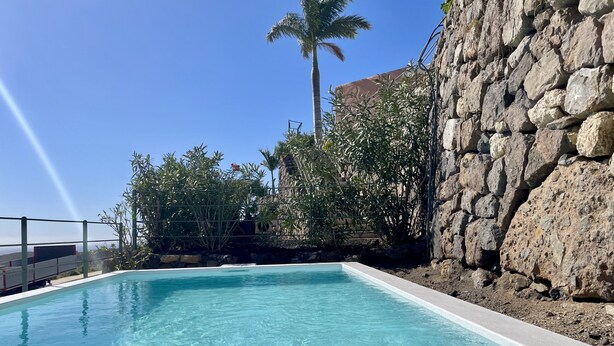 Une piscine d’un bleu éclatant, bordée d’un mur de pierre, avec des palmiers en arrière-plan.