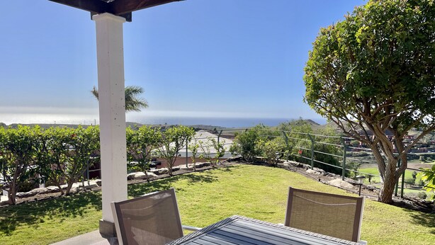 Um pátio com mesa e cadeiras, com vista para uma área gramada e o oceano.