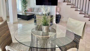 Uma sala de estar moderna com uma mesa de centro de vidro, cadeiras de vime, um sofá e uma televisão de tela plana na parede.