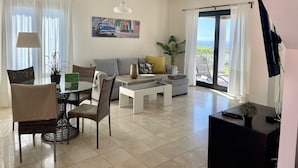 Uma sala de estar moderna com área de jantar, sofá, mesa de centro e televisão.