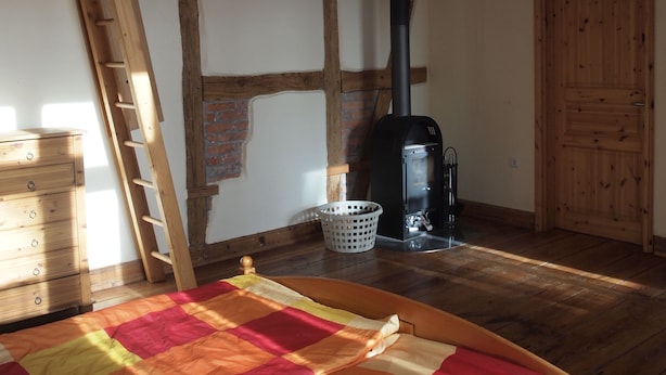 Een gezellige kamer met een hoogslaper, een houten trap, een bakstenen muur, een zwart houtkacheltje en een houten deur.