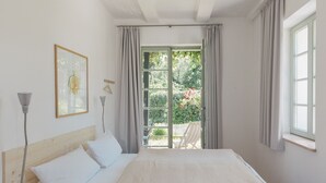 A bedroom with a bed, a window, and a view of a garden.