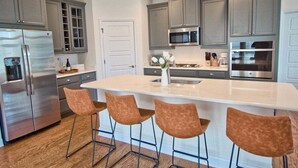 Una cocina moderna con gabinetes grises, electrodomésticos de acero inoxidable y una isla central con taburetes de bar.