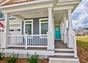 A two-story house with a covered porch, a blue door, and a small front yard.
