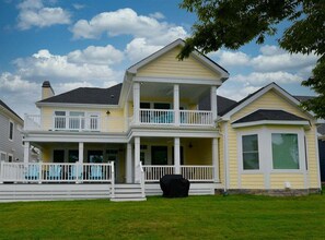 A two-story house with a porch, a covered grill, and a large window. - Bayside * 5BR New Luxury House (Selbyville)