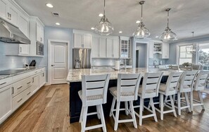 A modern kitchen with white cabinetry, a central island with bar stools, and pendant lighting. - Bayside * 5BR New Luxury House (Selbyville)