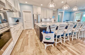 A modern kitchen with white cabinets, stainless steel appliances, and a central island with bar stools. - Bayside * 5BR New Luxury House (Selbyville)