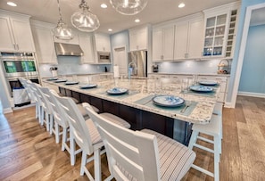 A kitchen with white cabinets, a large island with bar stools, stainless steel appliances, and pendant lighting. - Bayside * 5BR New Luxury House (Selbyville)