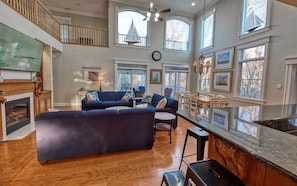 A spacious living room with a large blue sectional sofa, a fireplace, and a high ceiling with large windows.