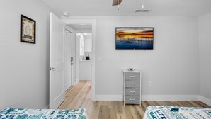 Quarto com duas camas, cômoda, pintura e ventilador de teto.