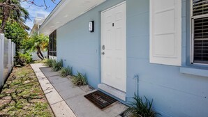 A light blue building with a white door marked 'B', a small welcome mat, and a window with blinds. - Dog-Friendly 4 Mins to the Beach and Pine Ave - A Place in Paradise Unit B (Anna Maria)