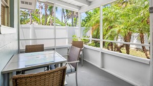 A covered patio with a table and chairs, large windows, and a view of palm trees. - Dog-Friendly 4 Mins to the Beach and Pine Ave - A Place in Paradise Unit B (Anna Maria)