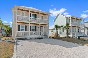 A two-story beachfront property with a covered porch and a gravel driveway.