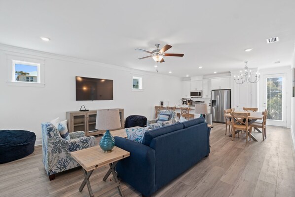A modern living room with a blue sofa, patterned armchairs, a wooden coffee table, and a ceiling fan.
